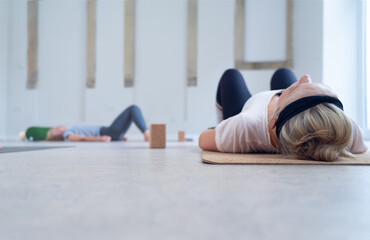 Naklejka premium Two women lying on a mat, eyes closed, meditating, during an indoor yoga class.