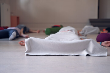 People lying on the floor, with their legs and feet covered by a blanket, while meditating, at the...
