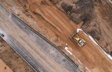 Dozer levels the ground during road construction, aerial view. Compaction of soil for laying asphalt at a construction site. The base course in pavements is a layer of material in a road way. © MaxSafaniuk