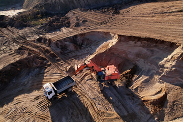 Mining excavator load the sand into dump truck in open pit. Developing the sand in the opencast. Heavy machinery on earthworks in quarry. Mining truck transports sand from open-pit mining.