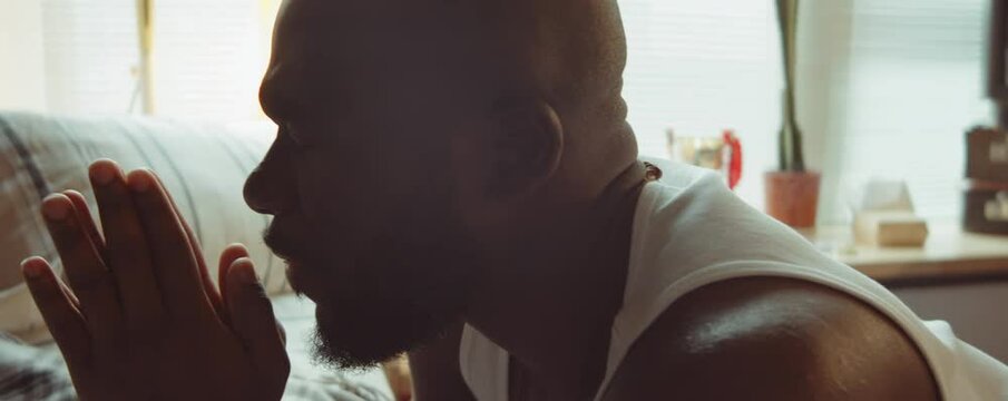 Close up tilt down shot of African American man holding hands clasped and saying prayers at home