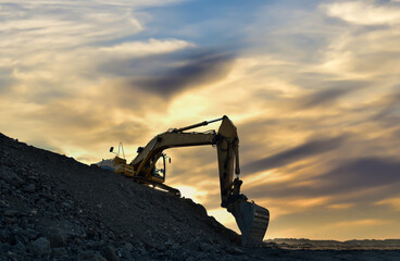 Fototapeta premium Excavator on earthmoving in open pit mining on sunset background. Backhoe digs sand and gravel in quarry. Heavy construction equipment during excavation at construction site.