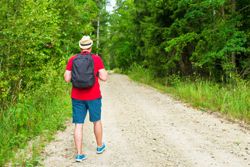 Back view of young man with backpack traveling alone forest on warm summer day.Tourism and active lifestyle concept.