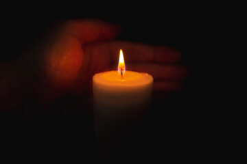 Obraz na płótnie Canvas One palm take care of candle fire at night.Selective focus,Dark black background.Closeup.