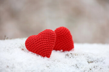 Fototapeta premium Two knitted red hearts in the snow in a park. Valentine's card, symbols of love, background for romantic event in winter, Christmas celebration