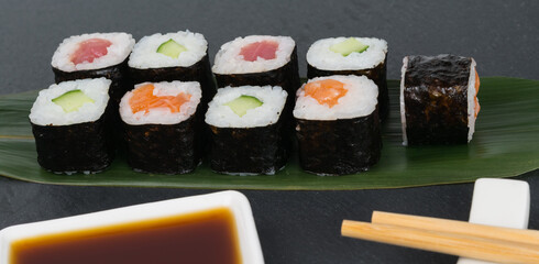 on the table, on a bamboo leaf, colorful rolls with fish and vegetables, soy sauce and chopsticks, a close-up of everything