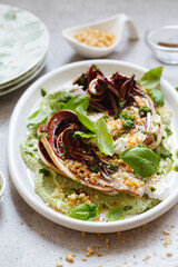 roasted radicchio salad with feta, green tahini, Pine nuts and basil pesto. Radicchio rosso di treviso tardivo, italian red chicory. Healthy Meal recipe preparation. Plant-based dishes.
