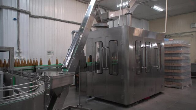 Medium shot of grey metallic bottling line. Orange-colored sea-buckthorn juice in glass bottles