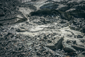 Scenic landscape with mountain river beginning from glacier among large moraines. Beautiful scenery with glacier at source of river. Mountain creek from ice among big stones. River source from glacier
