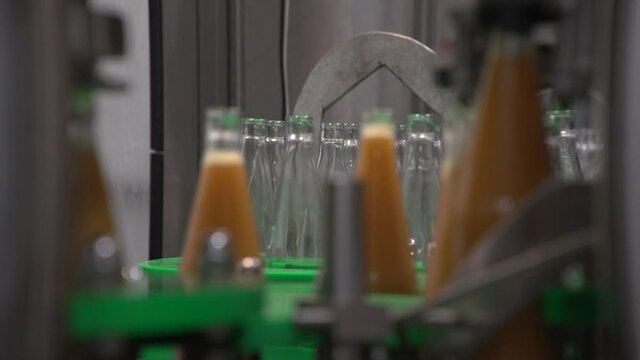 Close up of moving glass bottles inside bottling line. Filled sea-buckthorn juice bottles in foreground, empty bottles in background. Refocusing from filled bottles to empty ones and opposite way
