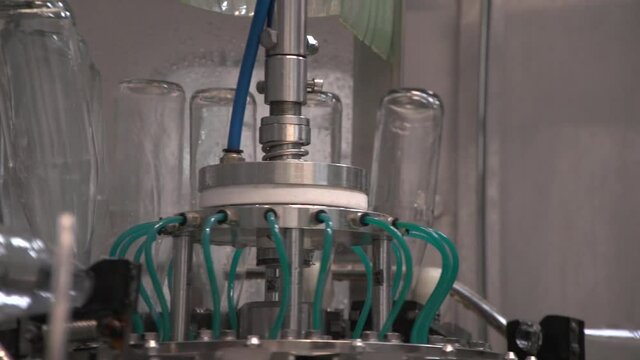Close up of mechanism bottling line moving and washing empty glass bottles to fill it with sea-buckthorn juice then. Panning moving bottles