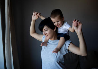 a young woman is holding her little son on her shoulders. family portrait