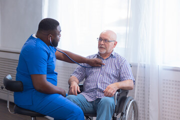 Caregiver and old man in a wheelchair. Professional nurse and patient in a nursing home. Assistance, rehabilitation and health care.