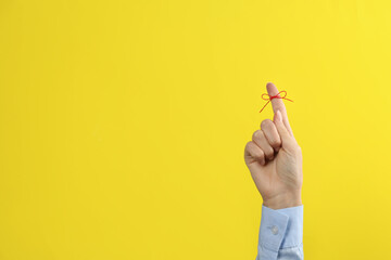 Woman showing index finger with tied red bow as reminder on yellow background, closeup. Space for text