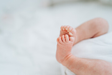 Obraz na płótnie Canvas Close bare feet of newborn unrecognizable child in white clothes on light blanket. Skin care, baby care
