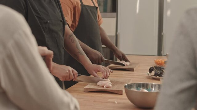 Tilting up of female African American chef cutting raw chicken fillet with knife on cutting board, teaching students in professional kitchen in culinary school