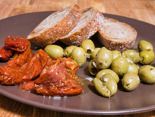 Mediterranean snacks. Plate with green olives, sun-dried tomatoes and slices of bread. Focus on the foreground