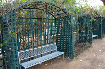 gray metal benches hidden in the arcade. green lattice trellises in a row along the way. Park with...