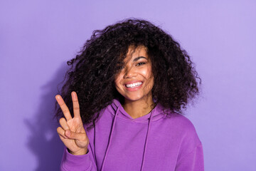 Photo of satisfied adorable girl toothy smile fingers make v-sign look camera isolated on purple...