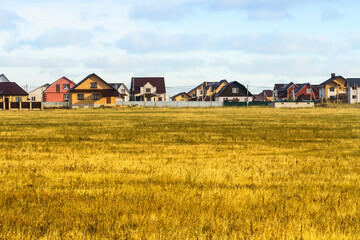 A lawn with green grass all the way to the horizon. Horizontal landscape of a flat field with fresh spring grass. Village, country houses, SNT, on the background of fields and trees.