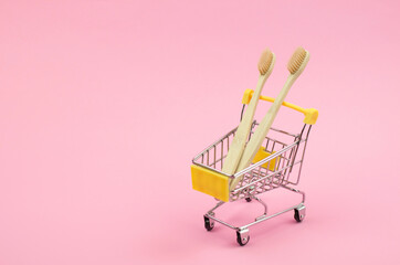 Two wooden toothbrushes in a shopping trolley on a yellow background