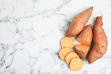 Whole and cut ripe sweet potatoes on white marble table, flat lay. Space for text