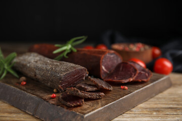 Delicious dry-cured beef basturma with rosemary and peppercorns on wooden table, closeup