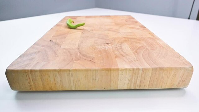 Slow motion footage of fresh colourful hot peppers falling and rolling to a wooden cutting board 
