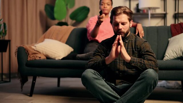 Young attractive guy meditate and looking at the camera while his girlfriend watching TV. Hobbies. Leisure time. High quality 4k footage