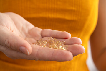 Closeup of woman hand and vitamin D capsules against bright yellow shirt.Concept of deficiency of...