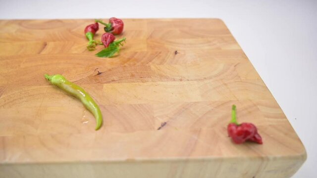 Slow motion footage of fresh colourful hot peppers falling and rolling to a wooden cutting board 
