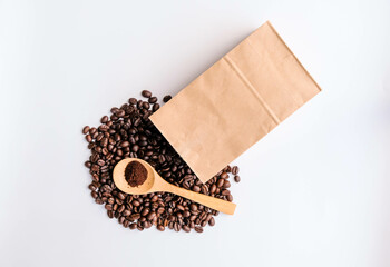 Coffee beans on white background from a paper coffee bag. Roasted coffee beans in wooden spoon on the wooden table top. Top view from space for your advertising.
