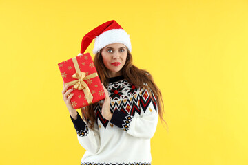 Attractive woman in Santa hat holds gift box on yellow background