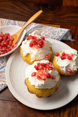 Top view of three muffins with cream cheese and pomegranate seeds on wooden table with bowl with pomegranate seeds and spoon, selective focus, vertical