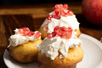 Close-up of three homemade muffins with cream cheese and pomegranate seeds, selective focus, on wooden table, horizontal, with copy space