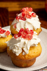 Top view of homemade muffins with cream cheese and pomegranate seeds, selective focus, on white plate, on wooden table, vertical