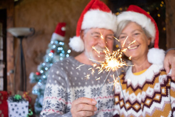 Defocused senior couple in Santa hats smiling and hugging at home at Christmas time with sparklers. Christmas Family Love concept