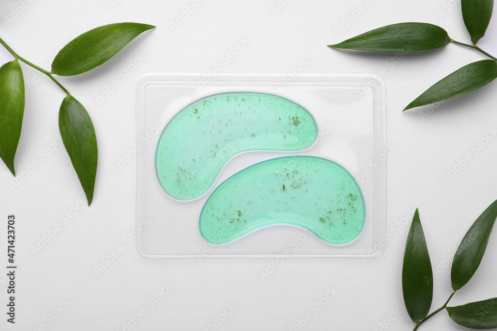 Wall mural Package with under eye patches and green twigs on white background, flat lay. Cosmetic product