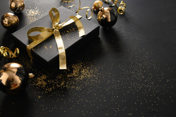 Gold and black gift and baubles on black background with Christmas decorations. Close up. Space for...