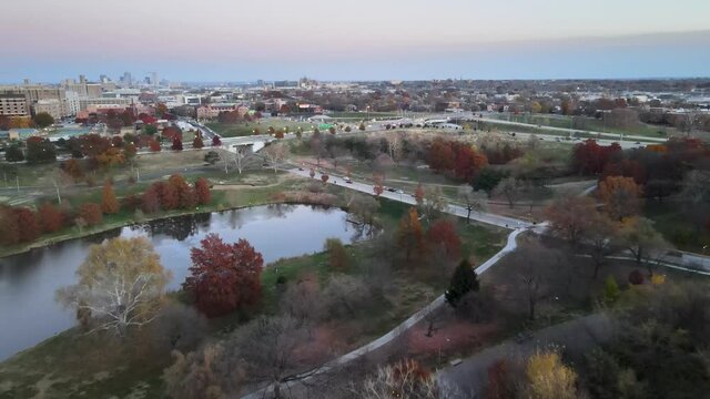 Forward drone shot of autumn colored trees over the pond with I-64 In the background during sunset shot at Forest Park, St. Louis, MO