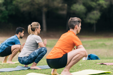 Three people squatting while doing yoga in a park