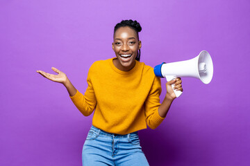 Young smiling African-American woman holding megaphone with another hand open in purple studio...