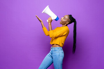 African American woman speaking on megaphone and pointing hand up in isolated purple studio background - obrazy, fototapety, plakaty