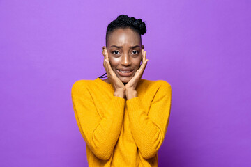 Young African-American woman feeling fear and frightened with hands on cheeks in purple isolated studio background - Powered by Adobe