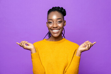 Portrait of smiling young African American woman pointing hands aside in isolated purple studio...