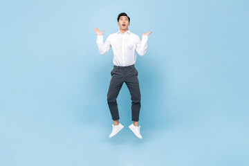 Young Asian man jumping with open palms and looking up in isolated light blue color background
