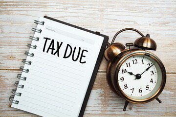 Tax due text on notepad with alarm clock on wooden background