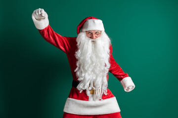 Funny actor in costume of Santa Claus with long beard gesturing while dancing on green background