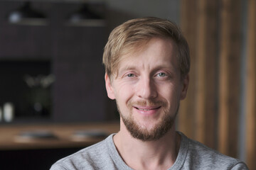 Closeup portrait of smiling European blonde guy posing at luxury apartment loft interior. Face of...
