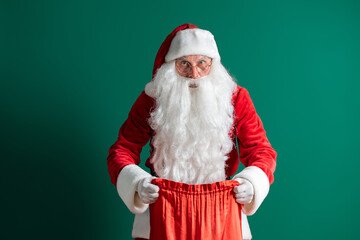 Fototapeta na wymiar Christmas time. Santa Claus holds and opens a bag of gifts on green background. New Year concept.